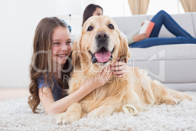 Girl embracing Golden Retriever while lying on rug