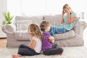 Angry siblings sitting arms crossed with upset mother on sofa