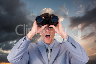 Composite image of suprised businessman looking through binocula