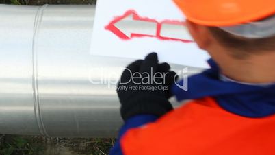 Worker draws red arrow on pipes