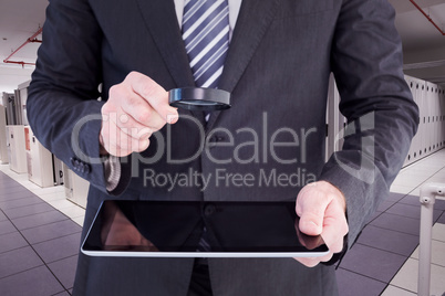 Composite image of businessman looking at tablet with magnifying