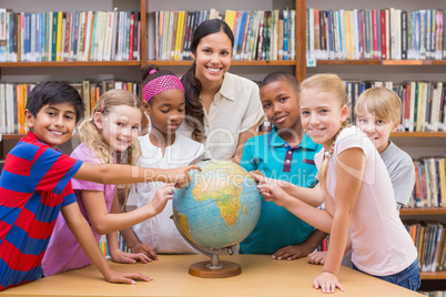 Cute pupils and teacher looking at globe in library