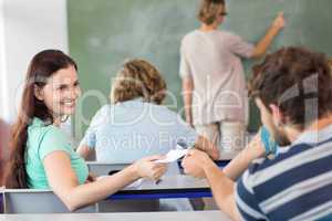 Female student passing note to friend in classroom