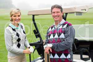 Happy golfing couple with golf buggy behind