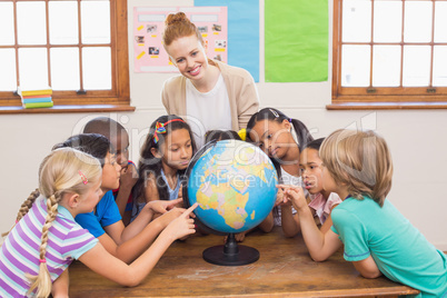 Cute pupils and teacher in classroom with globe