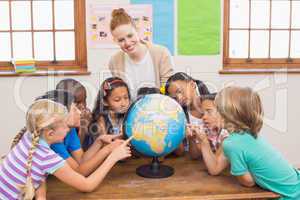 Cute pupils and teacher in classroom with globe