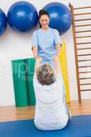 Therapist working with senior woman on exercise mat