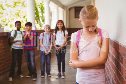 Sad schoolgirl with friends in background at school corridor