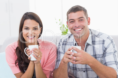 Happy couple holding coffee mugs at home