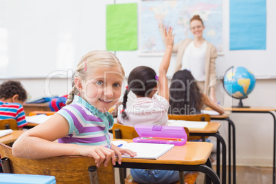 Cute pupil smiling at camera at his desk in classroom