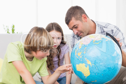 Children exploring globe while sitting with father