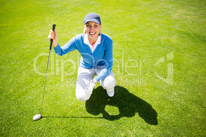 Smiling lady golfer kneeling on the putting green