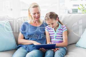 Mother with daughter using digital tablet on sofa