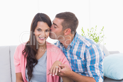 Man kissing woman wearing engagement ring