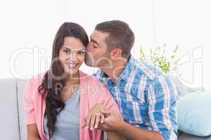 Man kissing woman wearing engagement ring
