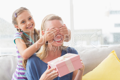 Mother holding gift with daughter covering her eyes