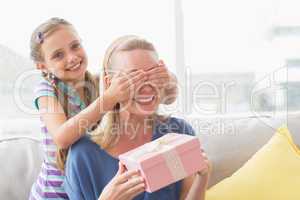 Mother holding gift with daughter covering her eyes