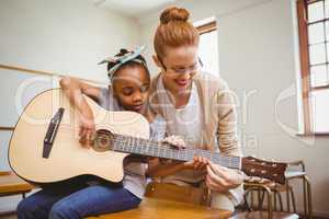 Teacher teaching girl to play guitar in classroom
