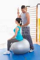 Trainer assisting woman exercising on fitness ball