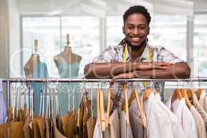 Male fashion designer leaning on rack of clothes