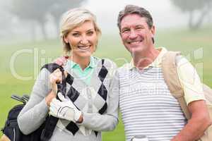 Golfing couple smiling and holding clubs