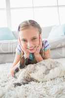 Happy girl with rabbit lying on rug in living room