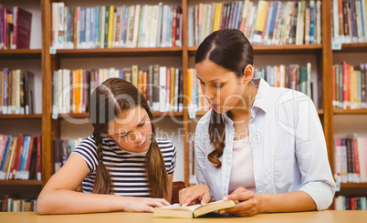 Teacher and girl reading book in library