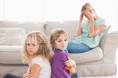 Angry siblings sitting arms crossed with sad mother on sofa