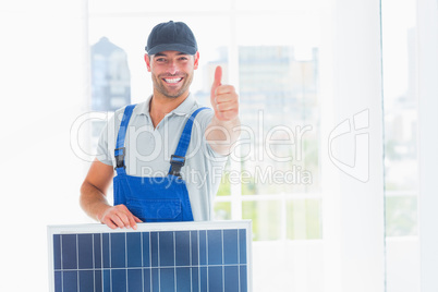 Workman with solar panel gesturing thumbs up in bright office