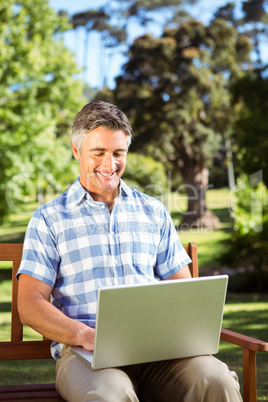 Man sitting on park bench using laptop