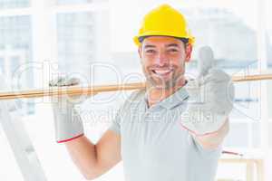 Handyman carrying wood while gesturing thumbs up