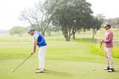 Golfer swinging his club with friend behind him