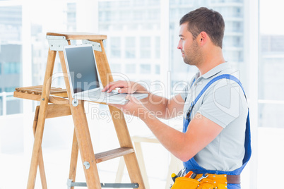 Handyman using laptop by ladder in bright office