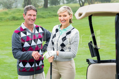 Happy golfing couple with golf buggy beside