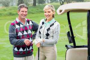 Happy golfing couple with golf buggy beside
