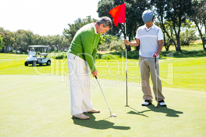 Golfer holding hole flag for friend putting ball