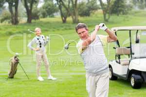 Golfer about to tee off with partner behind him