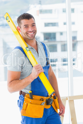 Happy repairman in overalls holding spirit level in office
