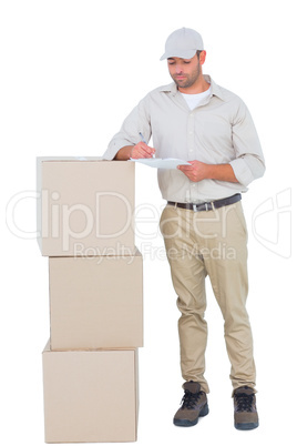 Delivery man writing on clipboard while standing by stacked boxe