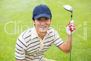 Crouching golfer smiling at camera and holding club