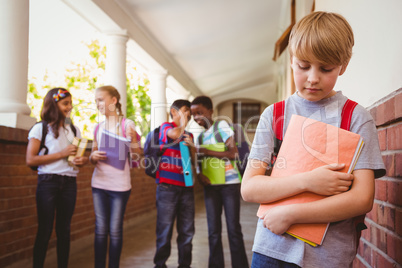 Sad schoolboy with friends in background at school corridor