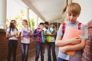 Sad schoolboy with friends in background at school corridor