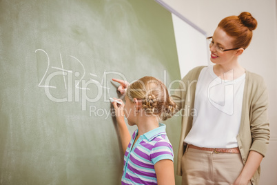 Teacher assisting girl to write on blackboard in classroom