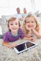 Siblings with digital tablet lying on rug