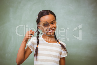 Little girl holding magnifying glass in classroom