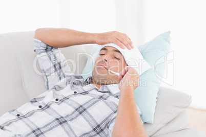 Man measuring temperature on thermometer on sofa