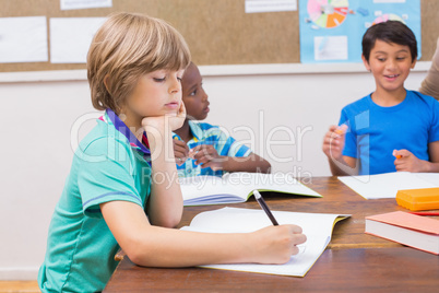 Cute pupils writing at desk in classroom