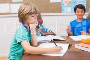 Cute pupils writing at desk in classroom