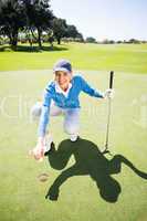 Smiling lady golfer kneeling on the putting green