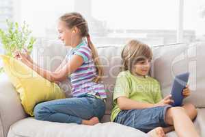 Siblings using technologies on sofa